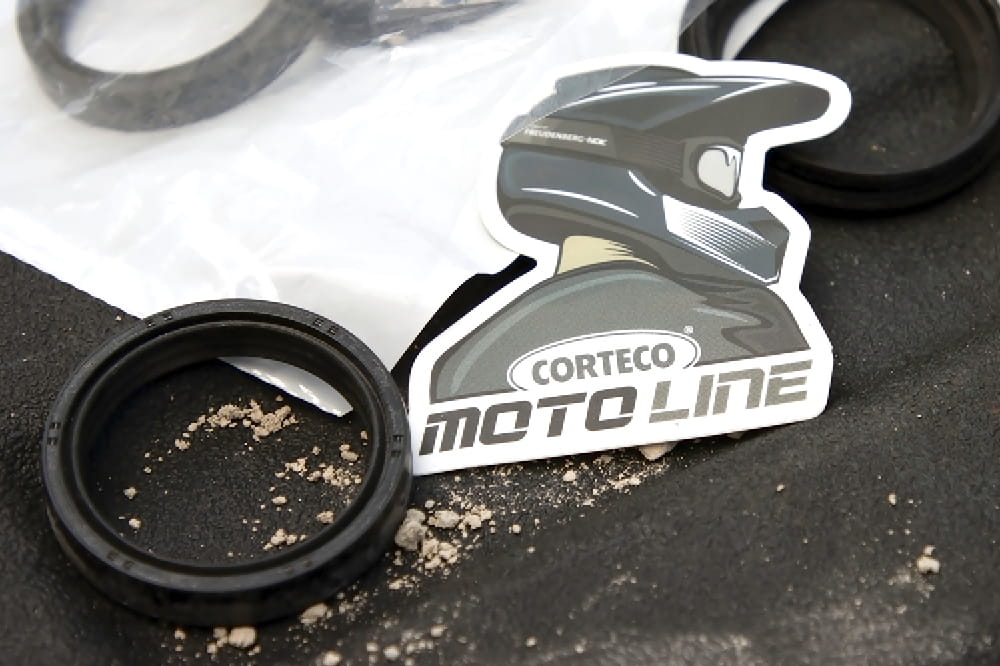 A sticker of a person with a motorcycle helmet on their head with the inscription Corteco Moto Line is lying on a table next to a seal. 