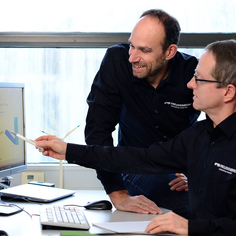 Two gentlemen in Freudenberg shirts look together at a screen with a seal cross section