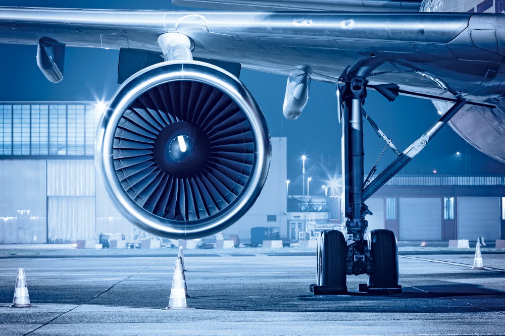 Turbine eines Flugzeuges ist im Fokus und im Hintergrund ist ein Flugplatz