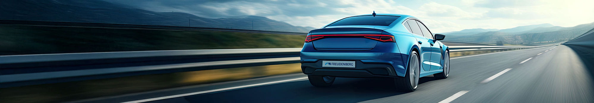 Ein blaues Auto fährt auf einer leeren Autobahn unter einem teilweise bewölkten Himmel, in der Ferne sind Berge zu sehen.