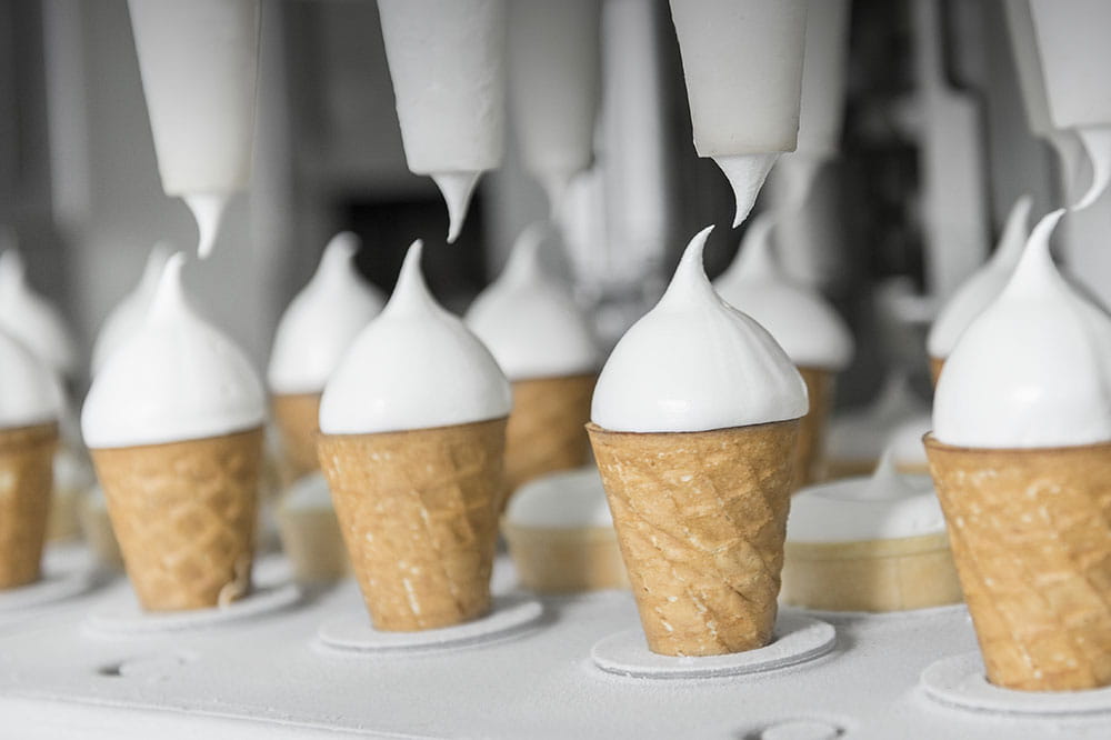 Eistüten sind in einer Vorrichtung und mit Spritzgerät wird die Eiscreme auf die Eistüte gesetzt