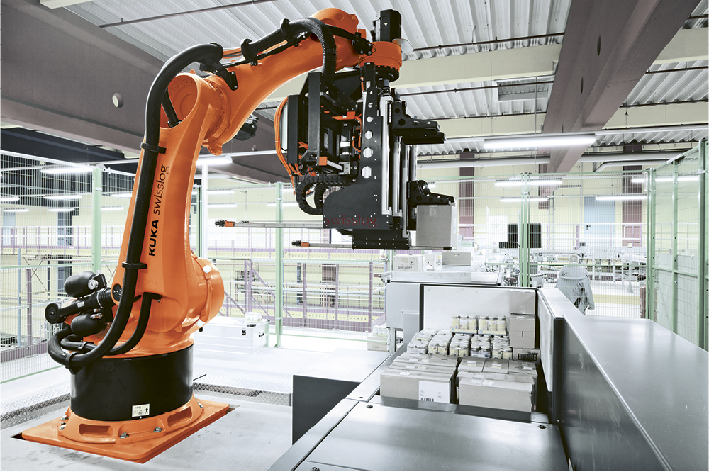Orangener Roboterarm stapelt kleine Pakete in einer Fabrik