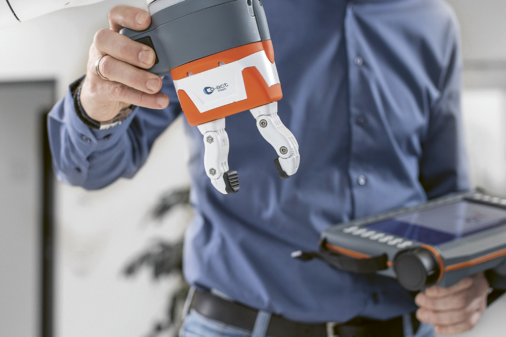 Ein Mann bedient mit einem Tablet den Greifarm eines Roboters