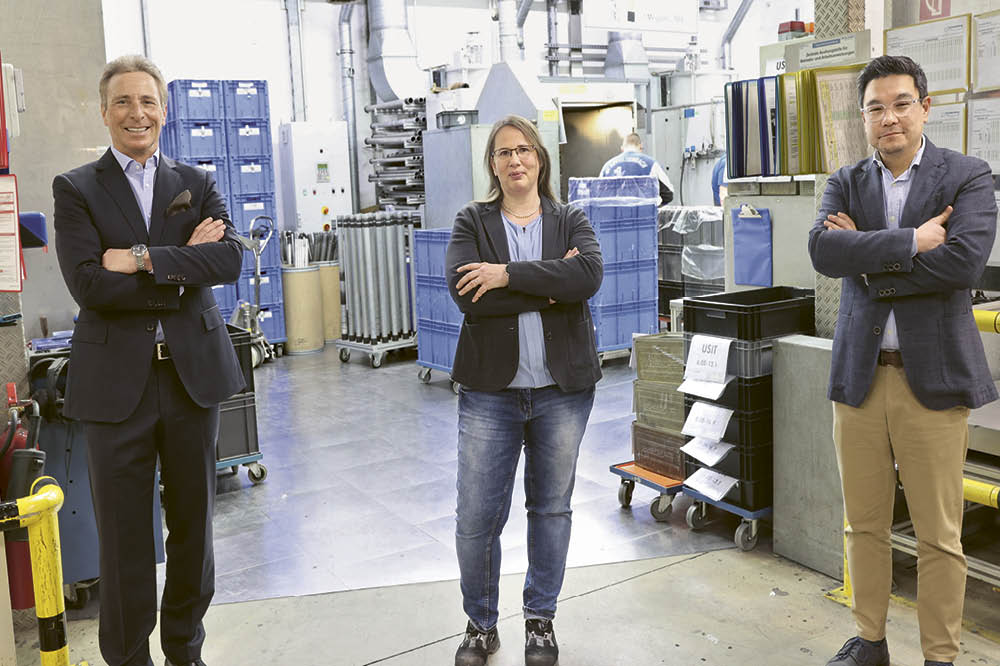 Ralf Schmid, Annette Reisner-Schaab und Dr. Clemens Elliger stehen in einer Reihe in der Fabrik.