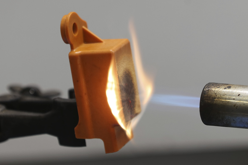 Ein Brenner wirft eine Flamme auf ein organgenes Stück Plastik, das ankokelt aber nicht schmilzt.