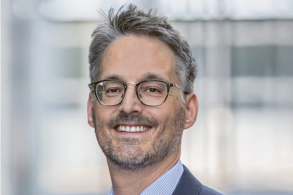 Porträt von David Koch, einem grauhaarigen Mann mit Bart und Brille. 