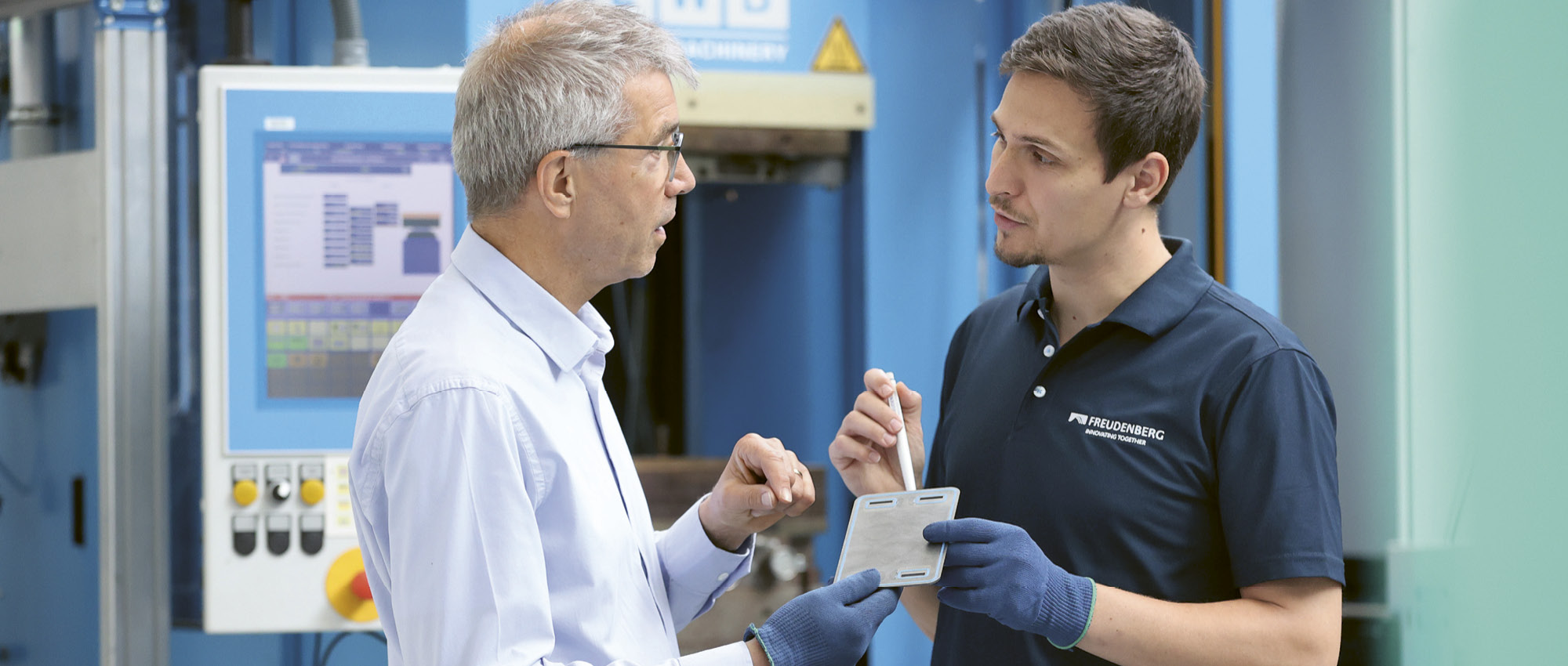 Zwei Männer stehen in einer Fabrik und unterhalten sich.