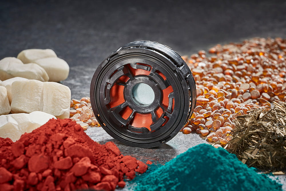 Schwarzes rundes Teil, umgeben von Haufen farbiger Pulver und Rohmaterialien.