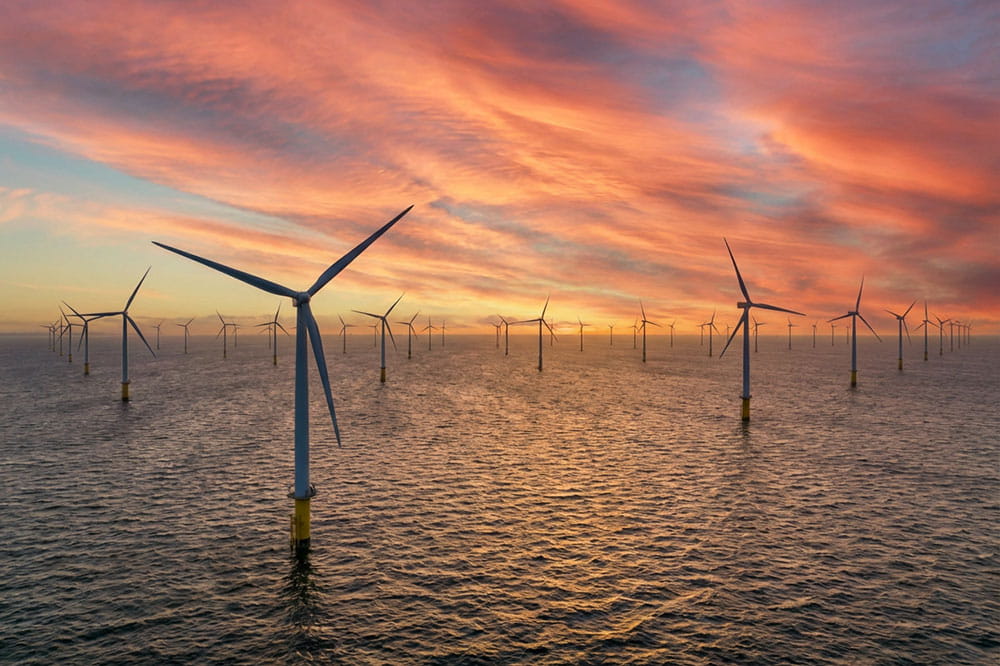 Mehrere Windräder, die nachhaltige erneuerbare Energie in einem Offshore-Windpark, während des Sonnenuntergangs produzieren