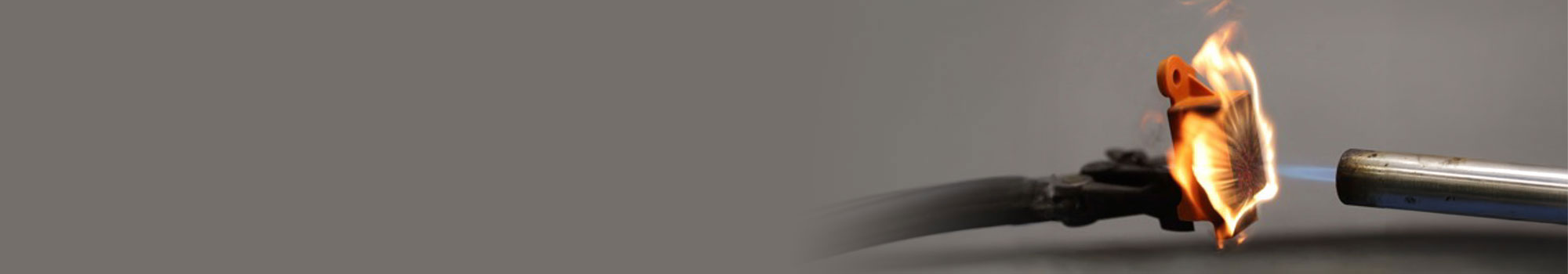 Wärmebeständigkeit Test: Ein Metallstab mit einer blauen Flamme erhitzt einen festgeklemmten Gegenstand, wodurch dieser Feuer fängt.